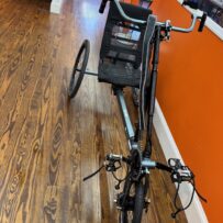 Front view of a used Berkel Bike Pro adaptive hand‑and‑foot cycle showing the crankset, pedals, and front wheel against a wood floor.