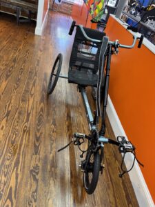 Front view of a used Berkel Bike Pro adaptive hand‑and‑foot cycle showing the crankset, pedals, and front wheel against a wood floor.