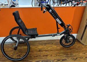 Side view of a used Berkel Bike Pro adaptive hand‑and‑foot cycle showing the crankset, pedals, and front wheel against a wood floor.